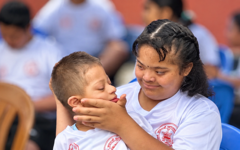 Special Olympics athlete sitting with a young child at an outdoor gathering
